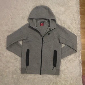 Grå Nike Tech  - Säljer en stilren grå  Nike Tech Hoodie med dragkedja och svarta detaljer. 
