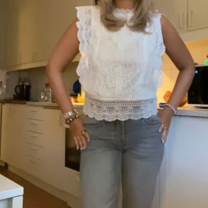Vit spetsblus - Säljer en vacker vit spetsblus med volangdetaljer. Blusen är ärmlös och har en fin, broderad design med en rak passform. Perfekt för en somrig look!