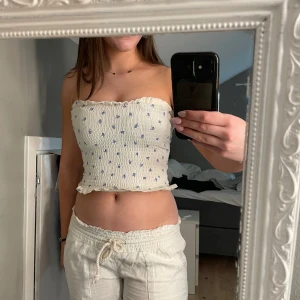 Vit tubtopp med blå blommor från H&M - Söt vit tubtopp från H&M med små blå blommor och volangdetaljer upptill och nedtill. Perfekt för sommardagar och kan enkelt matchas med olika outfits. 💙