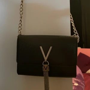 Svart axelväska med kedja - Snygg svart axelväska från Valentino i skinn med en elegant kedja som axelrem. Kedjan går även att förkorta.  Perfekt för att ge en stilren touch till din outfit.