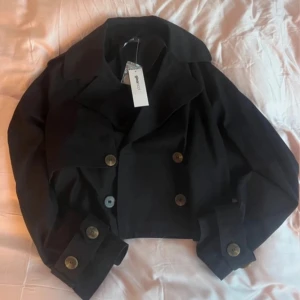 Svart kort trenchcoat från Gina Tricot - Säljer en stilren svart kort trenchcoat från Gina Tricot. Jackan har stora knappar och en klassisk krage. Perfekt för en trendig look. Nypris 599kr💕💕🎀