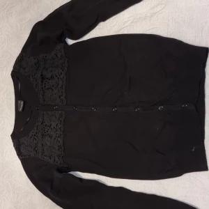 Svart kofta med spetsdetaljer, st S - Elegant svart kofta med spetsdetaljer över axlarna och knäppning framtill. Perfekt för en stilren look. Mkt fint skick