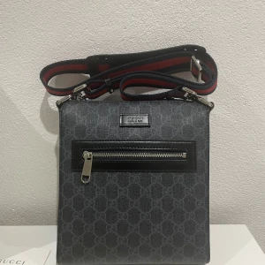 Gucci väska - Snygg GG Supreme messenger väska från Gucci, med ett diskret mönster och en praktisk dragkedja framtill. Väskan har en justerbar axelrem i rött och blått, vilket ger en stilren kontrast. Perfekt för att bära dina nödvändigheter med stil. Kommer med dustbag, kvitto, påse, dat dokument, och ett brev. Väskan är storlek S och var köpt i London. Originalpris 795£, mitt pris 3000kr.Den är storlek S. Mvh
