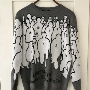 Grå tröja från Louis Vuitton - Unik grå tröja från Louis Vuitton med ett konstnärligt mönster av silhuetter och nummer. Textdetaljer på baksidan med olika designroller. Perfekt för den som vill sticka ut med stil.