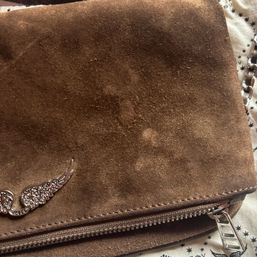 Snygg brun axelväska i mocka från Zadig & Voltaire. Två band följer med ett kortare och ett lite längre, och dustbag. De har lite små fläckar, eftersom jag inte har sakerna för att få bort de har jag inte provat tvätta, men de borde gå att tvätta bort. Laukut & Käsilaukut.