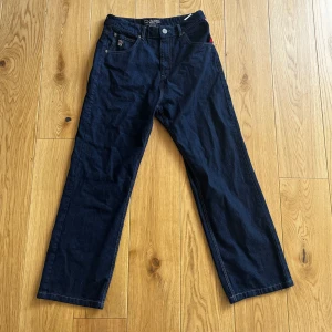 Mörkblå jeans från DNGRS - Snygga mörkblå jeans från DNGRS med broderad logga på bakfickan och kontrastsömmar. Klassisk femficksdesign med knappgylf och bälteshällor. Perfekta för en avslappnad stil.