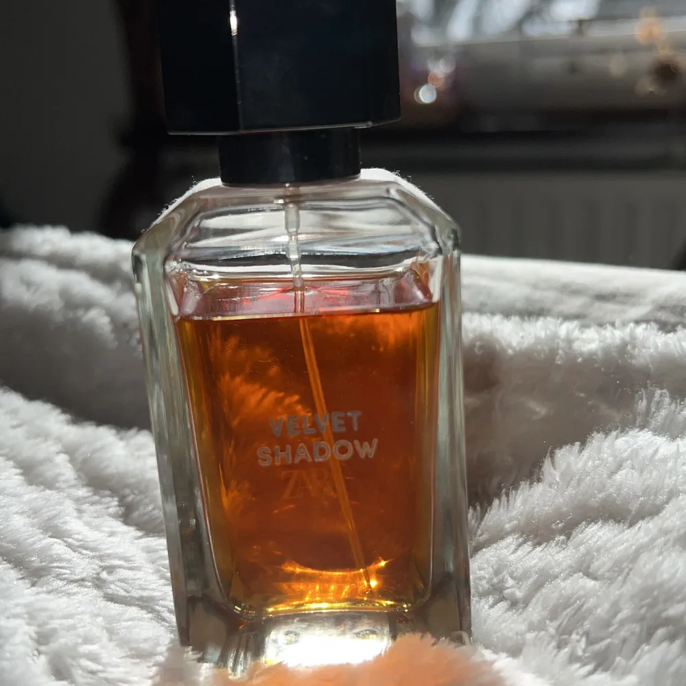 Elegant parfymflaska med en djup bärnstensfärgad vätska. Flaskan har en stilren, fyrkantig design med en svart, geometrisk kork. Namnet 'Velvet Shadow' är tryckt på framsidan. Jag skulle säga 80% är kvar av flaskan men du själv kan avgöra på bilden😍😍🙌🏼🍓. Perfume.