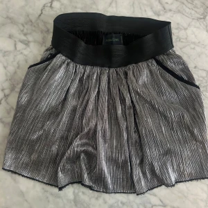 Silvrig Zadig & Voltaire minikjol! - Snygg silverfärgad minikjol från Zadig & Voltaire med en glittrig finish. Kjolen har en elastisk midja och ett plisserat tyg som ger en fin struktur. Den perfekta kjolen för en utekväll! Kan även användas som en snygg baneautopp! Använd endast en gång. Passar s-m, väldigt skön eftersom midjan är elastisk. Köpt för 3995kr för tre säsonger sedan, men säljer för 2000kr så väldigt bra pris!