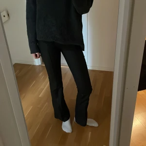 Svarta byxor från Nelly - Snygga svarta skinnbyxor från Nelly med låg midja och bootcut-stil. Byxorna har fejkfickor framtill och stängs med två knappar. Perfekta både till fest och vardag! 