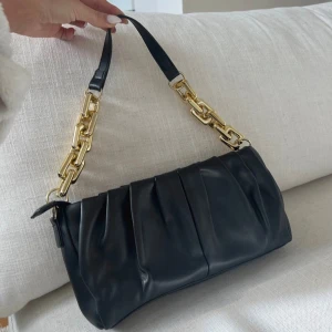 Svart axelväska med guldkedja - Snygg svart axelväska med guldkedja. Aldrig använd som ny. Säljer för 100 kr!