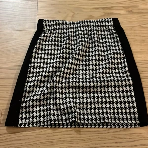 Svartvit rutig kjol - Snygg svartvit kjol med klassiskt hundtandsmönster. Kjolen har en kort längd och elastisk midja för bekväm passform. Perfekt för att ge en stilren touch till din outfit.