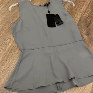 Grå ärmlös topp - Snygg grå ärmlös topp med en lätt utsvängd nederdel. Perfekt för en stilren look. Toppen har en dragkedja i ryggen för enkel på- och avtagning.