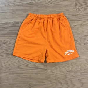 Orange shorts med tryck - Snygga orange shorts med elastisk midja och trycket 'California 90's' på benet. Perfekta för en avslappnad stil.