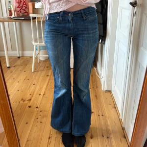 Blå bootcut jeans från Levi's - Snygga blå bootcut jeans från Levi's med klassisk femficksdesign och knappgylf. Perfekta för en avslappnad stil med en touch av retro. Levi's logga syns tydligt på bakfickan. Passar mig som brukar ha storleken 25/32.