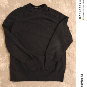 Mörkblå tröja från Boss - Säljer en stilren mörkgrå tröja från Boss. Tröjan har en klassisk design med rund hals och långa ärmar. Perfekt för en avslappnad men ändå elegant look. Passar bra till både jeans och chinos. L för barn.