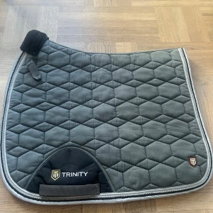 Mörkgrått trinity dressyrschabrak - Det är i superfint skick och använt max 3 gånger. Det är nytvättat så inte någon päls kvar. Tror att jag köpte det för ca 250kr så säljer nu för 100kr. Det är i storlek full men är lika stort som ett så som är i storlek cob, så skulle säga att det är ett litet full. Det är i dressyrmodell!