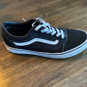 Svarta sneakers från Vans - Säljer ett par klassiska svarta Vans sneakers med snörning. Skorna har den ikoniska vita sidostripen. Perfekta för en avslappnad stil.