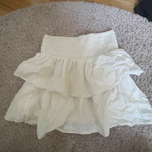 Vit kjol med volang - Charmig vit kjol med volangdetaljer och elastisk midja. Perfekt för en somrig look. Kan även användas som tub topp!!