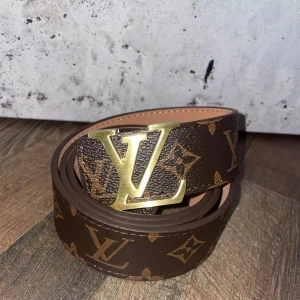 Brunt bälte från Louis Vuitton - Säljer ett stilrent brunt bälte från Louis Vuitton med det klassiska monogrammönstret. Bältet har en elegant guldspänne med LV-logotypen. Perfekt för att ge en lyxig touch till din outfit.