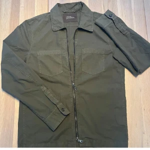 Olivgrön jacka från Oscar Jacobson - Snygg olivgrön jacka från Oscar Jacobson med dragkedja framtill och två bröstfickor. Jackan har långa ärmar och en klassisk krage. Perfekt för en stilren look. Skriv gärna dm vid frågor, är öppen för prisförslag.