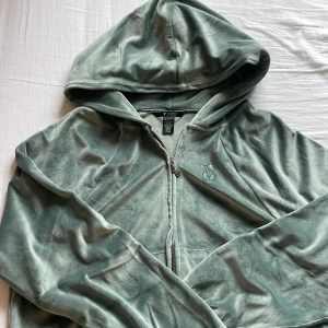 Grön velour hoodie Victoria's Secret - Mjuk och lyxig ljusgrön velour hoodie från Victoria's Secret med dragkedja och VS-logga broderad på bröstet. Tröjan har huva, känguruficka och snygg VS-detalj på dragkedjan. Perfekt för chill dagar eller när du vill vara extra cozy.