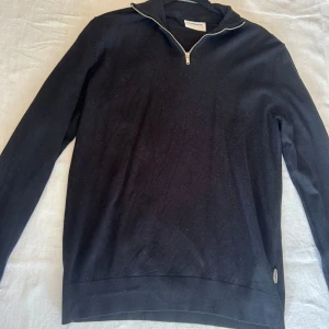 Svart half zip tröja från Lindbergh - Svart långärmad tröja från Lindbergh med half zip-dragkedja i halsen. Storlek M. Klassisk och stilren modell med ribbade muddar vid ärmslut och nederkant. Perfekt för lager-på-lager och funkar året runt. Mjuk och bekväm känsla.