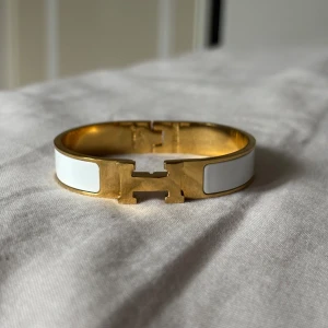 H armband - Snyggt H  armband i guldpläterad metall med vita emaljdetaljer. Armbandet har den ikoniska H-formade låset framtill. Pris kan diskuteras vid snabb affär.