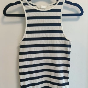 Randig ribbad linnetopp i marinblått - Snygg ärmlös linnetopp med horisontella marinblå och vita ränder. Ribbad struktur som ger en cool och sportig vibe. Rund halsringning och smal passform, perfekt för varma dagar eller lager på lager. Enkel att matcha med jeans eller shorts.