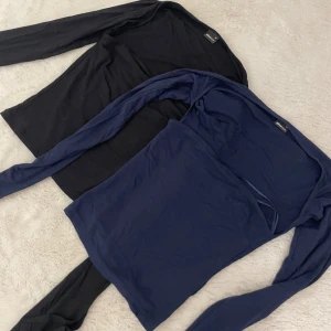 Två långärmade tröjor Gina Tricot - Två basic långärmade tröjor från Gina Tricot, en i svart och en i mörkblå. Båda har en enkel, tight passform och är gjorda i mjuk bomullsmix. Perfekta att styla med jeans eller kjol för en clean look. 