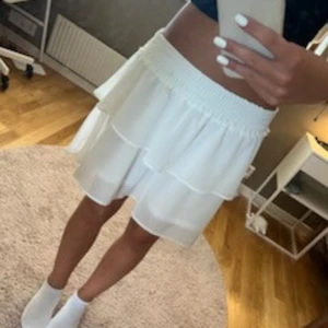 Vit volangkjol från Chelsea XS - Supersöt vit kortkjol från Chelsea i storlek XS. Kjolen har bred smock i midjan och volanger som ger en flowy och luftig känsla. Materialet känns lätt och svalt.