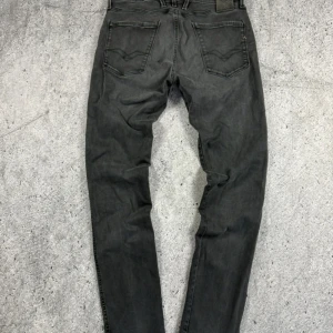 Replay Anbass svarta jeans, W33 L32 - Svarta Replay Anbass jeans med klassisk femficksdesign och diskreta sömmar på bakfickorna. Jeansen har en slim passform och är tillverkade i mjukt bomullsmaterial med lite stretch för extra komfort. Perfekta för dig som gillar en stilren look.