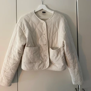 Quiltad beige jacka från Gina Tricot - Quiltad beige jacka från Gina Tricot med rund halsringning, stora fickor framtill och knäppning med knappar. Använd en gång