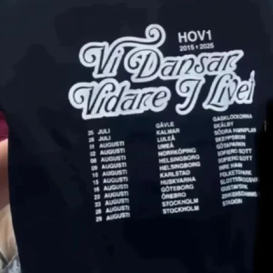 SÖKER - Svart t-shirt från Hov1 med stort vitt tryck på ryggen: 'Vi Dansar Vidare I Livet' och turnédatum samt städer. Klassisk passform och rund hals. Perfekt för dig som älskar svensk musik och vill visa din support för Hov1.