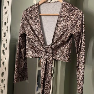 Leopardmönstrad omlottopp med knyt - Säljer en croppad leopardmönstrad omlottopp med långa ärmar och knyt framtill. Toppens material är stretchigt och mjukt, perfekt för att sticka ut. Djurmönstret går i beige och svart och ger en edgy vibe.