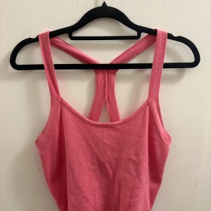 Rosa stickad linnetopp från New Yorker  - Säljer en rosa stickad linnetopp från new yorker i storlek M. Toppen har breda axelband och en snygg racerback-design i ryggen. Croppad modell som sitter tajt och är perfekt för varma dagar. Enkel och stilren utan mönster eller extra detaljer. 