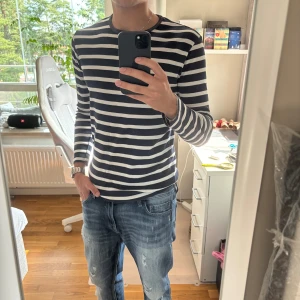 Blåvit randig långärmad tröja - Säljer en svartvit långärmad tröja med klassiskt horisontellt randigt mönster. Tröjan har rund hals och är i en normal passform, perfekt för dig som gillar enkel och stilren design. Passar till jeans eller shorts för en chill look.