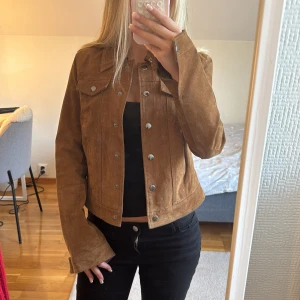 Brun mockajacka från Vero Moda - Snygg brun mockajacka från Vero Moda med klassisk jeansjacke-modell. Jackan har silvriga knappar framtill, två bröstfickor med lock och lång ärm. Den är i storlek S men är ganska liten i storlek så skylla säga att den är lite mer XS!