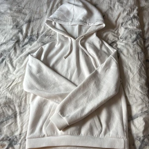 Vit hoodie från MNG med huva - Säljer en stilren vit hoodie från MNG i storlek S. Tröjan har en klassisk huva med snörning och en stor ficka framtill. Mjuk bomullskänsla och ribbade muddar vid ärmslut och nederkant. Perfekt för chill dagar eller när du vill ha en clean look. Obs finns en sminkfläck so mdu kan få bort på insidan