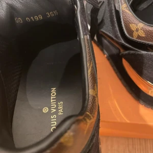 Louis Vuitton sneakers svart/guld 36,5 - Storlek 36,5 men passar 37/38. Snygga Louis Vuitton sneakers i svart med klassiskt monogrammönster i brunt och guldiga detaljer på hälen. Skorna har snörning, vit sula och robust LV-märkt yttersula. Materialmix av skinn, textil och mocka ger en lyxig känsla. 