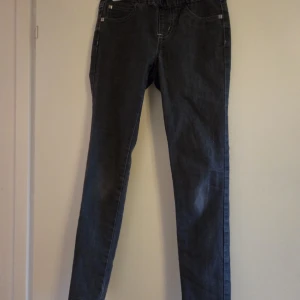 Mörkgrå jeans med resårmidja - Snygga mörkgrå jeans med resår i midjan och klassiska fem fickor. Jeansen har raka ben och kontrastsömmar, vilket ger en stilren look. Perfekta för dig som gillar bekväma och stilrena byxor i jeansmaterial.