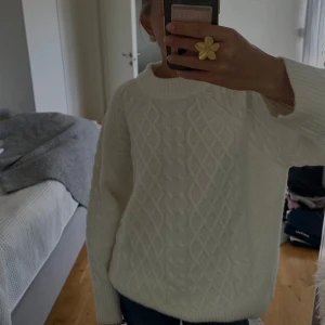 Vit stickad tröja från Lager 157 - Supermysig vit stickad tröja från Lager 157 med grovt kabelstickat mönster framtill och bred ribbad krage. Tröjan har lång ärm och en relaxed fit som är perfekt för kyliga dagar. Passar dig som gillar en klassisk men ändå trendig look!