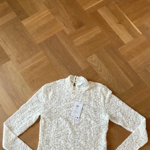 Vit spetsblus från VILA, storlek M - Säljer en vit långärmad blus från VILA i storlek M. Blusen har ett blommigt spetsmönster och en liten ståkrage. Baksidan har en knappdetalj med öppning vid nacken. Perfekt för dig som gillar romantiska och feminina detaljer.
