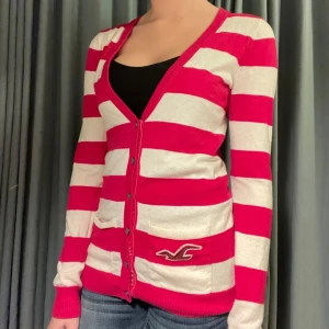 Rosa- och vitrandig kofta från Hollister - Säljer en snygg rosa- och vitrandig kofta från Hollister. Koftan har långa ärmar och knappar framtill. Använd fåtal gånger. Pris kan diskuteras💕