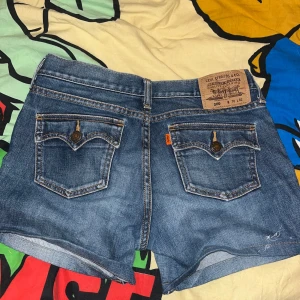 Levi's blå jeansshorts med fickor - Klassiska blå jeansshorts från Levi's med snygga bakfickor och ikonisk läderpatch. Shortsen har normal passform, fem fickor och slitna kanter för en chill vibe. Perfekta för varma dagar och enkel att matcha med allt.säljer då de är för stora.