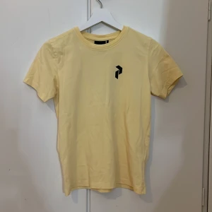 Gul Peak Performance t-shirt med tryck - Fräsch gul t-shirt från Peak Performance med svart grafiskt tryck både fram och bak. Klassisk rund hals och korta ärmar. Skön bomullskvalitet som känns mjuk mot huden. Perfekt för dig som gillar stilrena och sportiga plagg med en modern touch.