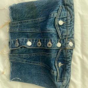 Blå jeanskjol från Zara med knappar - Säljer en blå jeanstopp från Zara med coola silverfärgade knappar framtill och fickdetaljer. Toppen har rå kant nedtill och smockad bakdel för extra stretch. Perfekt för dig som gillar streetstyle och denim.
