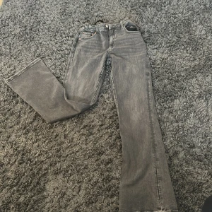 Grå bootcut jeans från Gina Tricot - Snygga grå jeans från Gina Tricot i storlek 164. Modellen har bootcut-ben och klassisk femficksdesign. Jeansen är i mjukt denimtyg och har justerbar midja med resår och knapp på insidan. Perfekta för dig som gillar en avslappnad men trendig look.