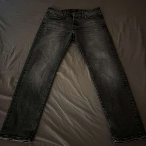 Mörk grå jeans från Jack & Jones - Snygga svarta jeans från Jack & Jones med klassisk femficksdesign och raka ben. Jeansen har en lätt tvättad look och är tillverkade i bomull med en skön passform. Perfekta för dig som gillar en stilren och enkel vibe.