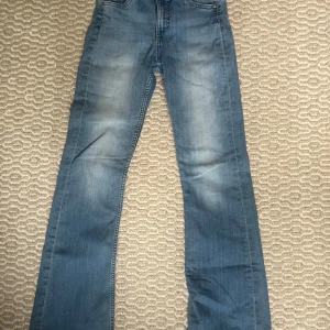 Blå bootcut jeans med slitna kanter - Snygga blå jeans med bootcut-modell och ljusa slitningar på låren. Jeansen har klassisk femficksdesign och råa, fransiga benslut för en avslappnad vibe. Perfekta för dig som gillar en retrostil och vill ha ett par jeans med lite edge. Dem har lite slitningar längs ner men de märks inte när man har på dem