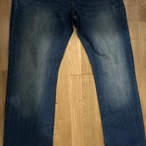 Blå jeans med straight fit - Snygga blå jeans med klassisk straight fit och lätt slitna detaljer på framsidan och baksidan. Jeansen har fem fickor och en mörk tvätt med ljusare partier. Perfekta för dig som gillar en enkel och tidlös stil.